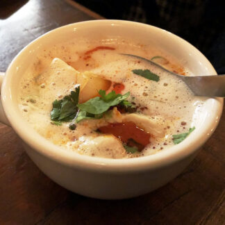 Coconut chicken soup with Enoki mushrooms, green onions, yellow onions, in a cup.