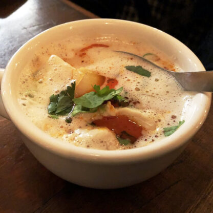 Coconut chicken soup with Enoki mushrooms, green onions, yellow onions, in a cup.