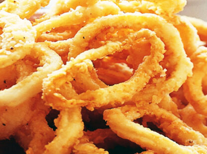 Fried onion rings with golden crispy breading and wavy texture in a bowl.