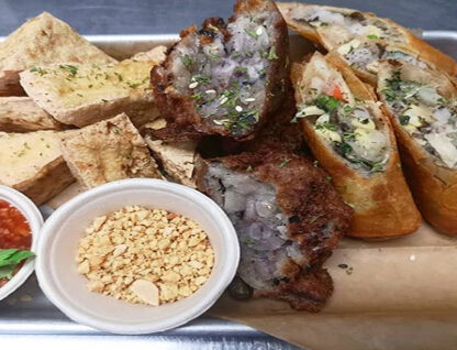 Fried tofu, spring rolls, fried meat patties, ground peanuts, and dipping sauce on a tray.