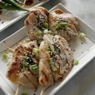 Grilled chicken thigh on wood skewers, topped with sesame seeds and teriyaki sauce on white plate