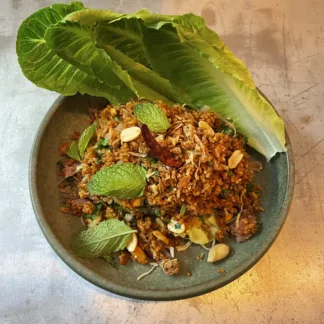 Crispy rice ball salad with sour sausage, peanuts, herbs, and lime on white plate, served with lettuce