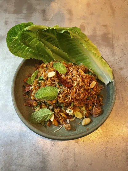 Crispy rice ball salad with sour sausage, peanuts, herbs, and lime on white plate, served with lettuce