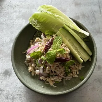 Larb chicken minced meat salad with lettuce wraps, herbs, and lime wedges