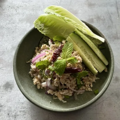 Larb chicken minced meat salad with lettuce wraps, herbs, and lime wedges