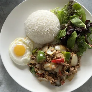 Thai basil stir-fry with ground chicken, onions, and bell peppers on a plate with jasmine rice, fried egg, and mixed greens.