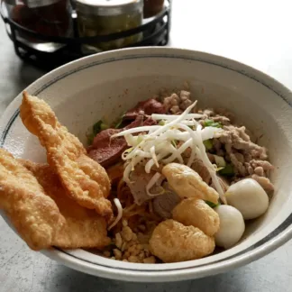 Dry tom yum noodles with ground pork, fish balls, pork liver, chili, peanuts, and bean sprouts in a bowl.