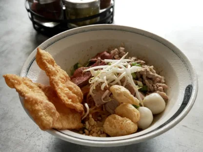 Dry tom yum noodles with ground pork, fish balls, pork liver, chili, peanuts, and bean sprouts in a bowl.