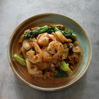 Stir-fried wide rice noodles with shrimp, egg, Chinese broccoli, and soy sauce served in a bowl