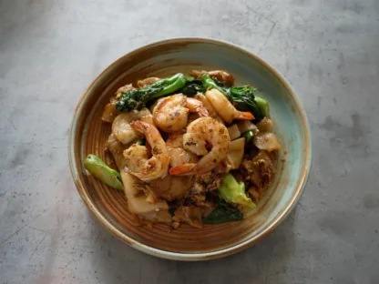 Stir-fried wide rice noodles with shrimp, egg, Chinese broccoli, and soy sauce served in a bowl