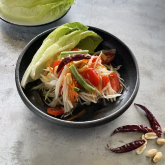 A salad with shredded green papaya, carrots, tomatoes, green beans, peanuts in a bowl and a side of lettuce.
