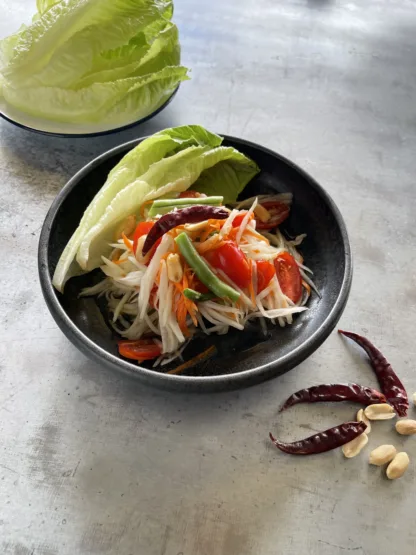 A salad with shredded green papaya, carrots, tomatoes, green beans, peanuts in a bowl and a side of lettuce.
