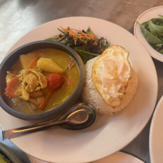Thai yellow curry with chicken and vegetables served in a bowl. Rice topped with a fried egg and a side greens on a plate.